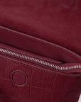 Close-up of a burgundy textured leather Mendy Bag showing a zippered compartment and circular seamless magnetic button detail.