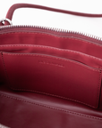 Close-up of the interior of a burgundy leather bag, showing a zippered opening, interior pocket, and debossed 'RICO RINALDI' branding on the lining.