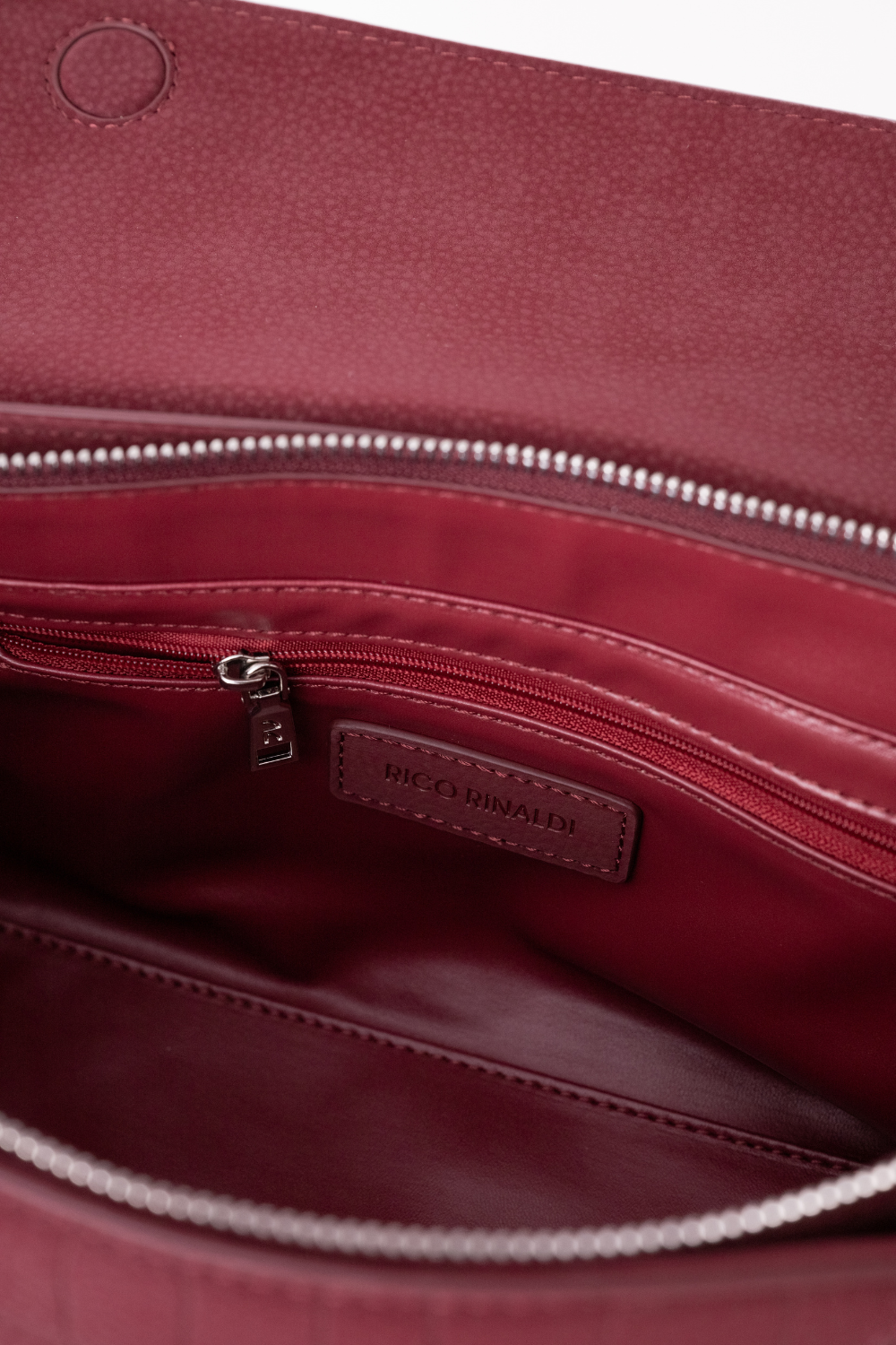 Close-up of the interior of a burgundy leather bag, showing a zippered pocket with a small leather brand label that reads 'RICO RINALDI'.