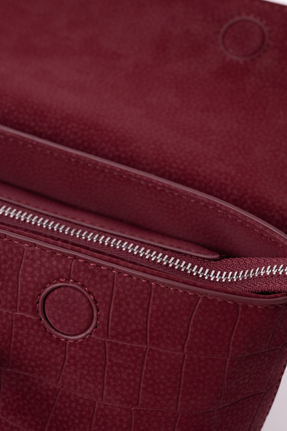 Close-up of a burgundy textured leather Mendy Bag showing a zippered compartment and circular seamless magnetic button detail.