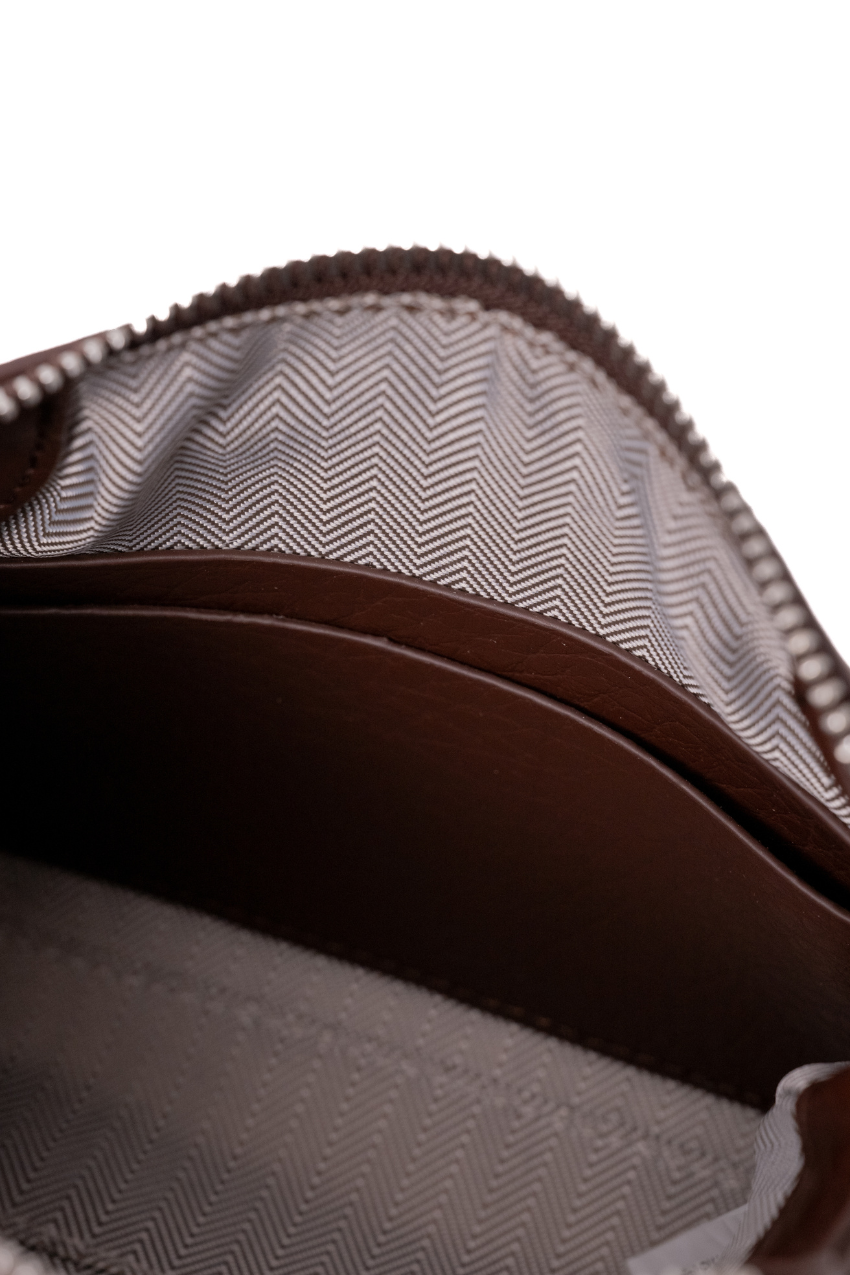 Close-up of the interior of a brown leather zippered pouch or wallet, showing a gray and white herringbone patterned lining. 2 pocket slot inside pouch. Coin pouch or card. Rico Rinaldi Malaysia.