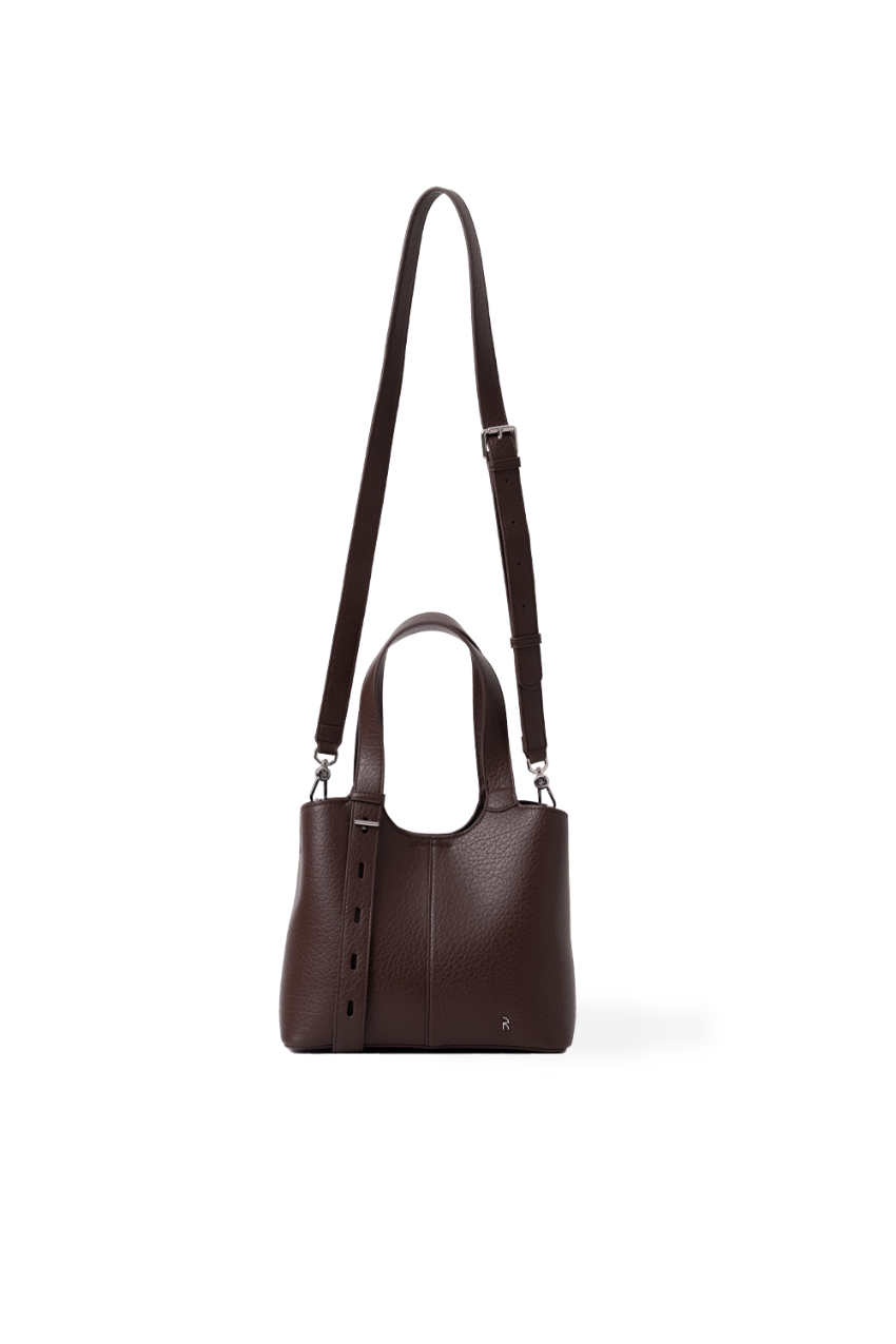 A dark brown pebbled leather handbag with a top handle, a long shoulder strap, and a vertical hanging strap detail, shown against a plain white background.