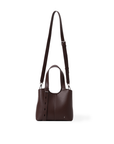 A dark brown pebbled leather handbag with a top handle, a long shoulder strap, and a vertical hanging strap detail, shown against a plain white background.