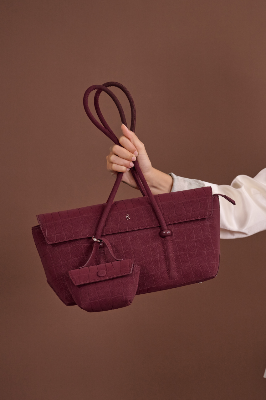 Woman holding Rico Rinaldi Mendy Deep Maroon shoulder bag, elegant East-West handbag for work, travel and everyday wear