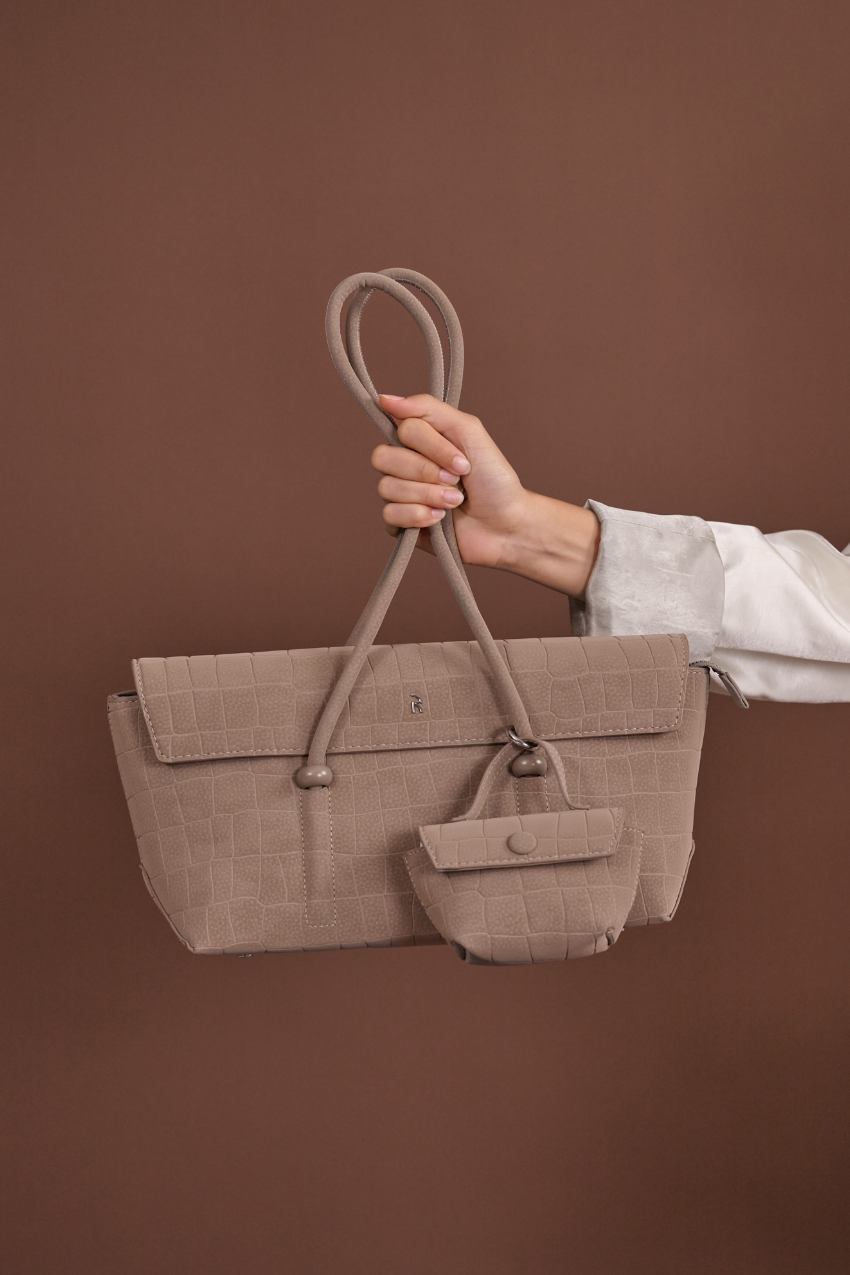 Woman holding Rico Rinaldi Mendy Latte shoulder bag, elegant East-West handbag for work, travel and everyday wear